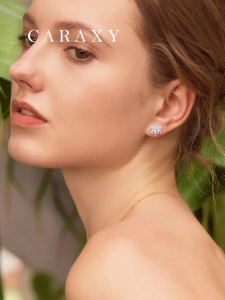 Close-up of a woman wearing a Caraxy snowflake diamond stud earring in a lush green setting.