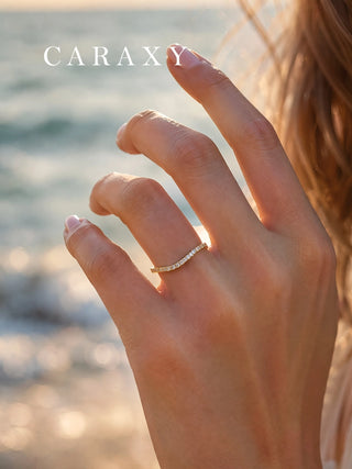Curved lab-grown diamond band in 18K yellow gold worn alone on a hand in warm beach light.