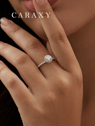 A brilliant halo engagement ring with pavé band worn on finger to show proportions.