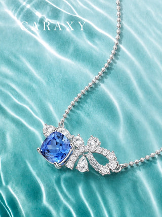 Lab-grown blue sapphire and diamond bow necklace displayed on blue water-inspired background