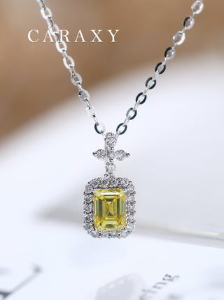 Close-up of a lab-grown emerald-cut fancy yellow diamond halo pendant necklace on a surface.