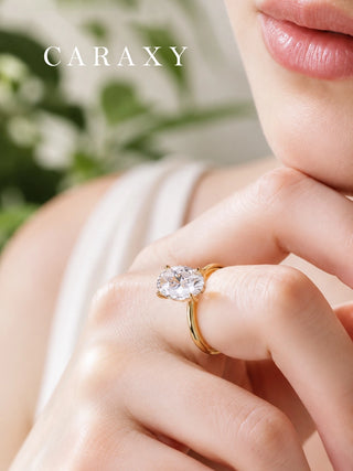 Close-up of CARAXY oval cut engagement ring worn on hand in yellow gold