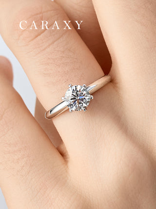 Close-up of a platinum six-prong solitaire engagement ring on finger to show scale.