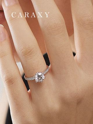 Close-up of a six-prong micro pavé engagement ring worn on finger to show scale.